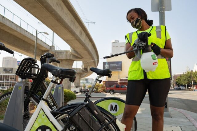 A brown, female Metro Bike Share employee cleans bikes while wearing a mask.